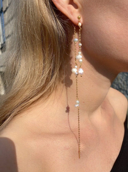 Lange, guldbelagte øreringe med kæder og perler i forskellige størrelser på en model.