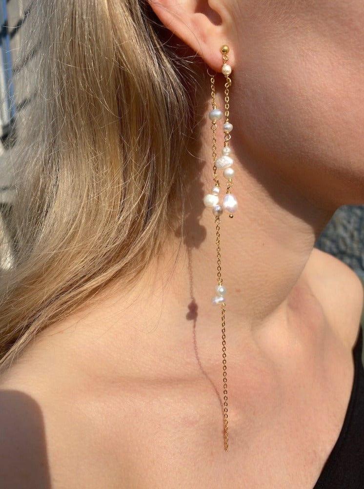 Lange, guldbelagte øreringe med kæder og perler i forskellige størrelser på en model.