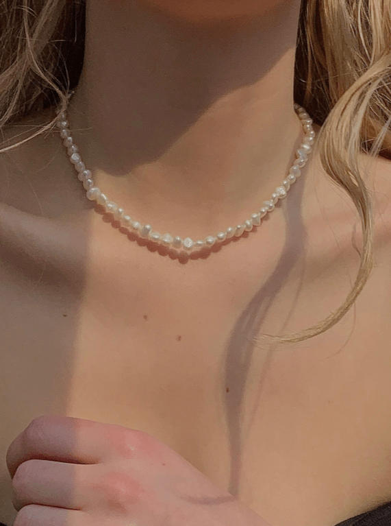 Halskæde af små, hvide perler om halsen på en person, elegant og delikat stil.