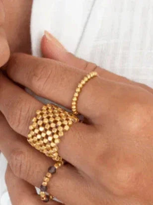 Hånd med guldbelagt ring af små kugler, enkel og tynd, blandt flere andre ringe.