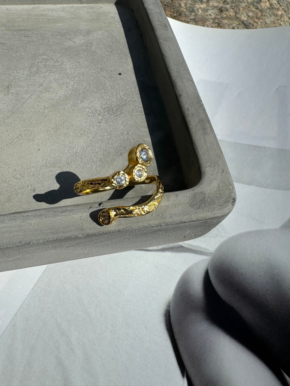 Elvira ring i 18 karat guldbelagt fra Andcopenhagen Jewelry med hvide sten, vist på grå bakke.