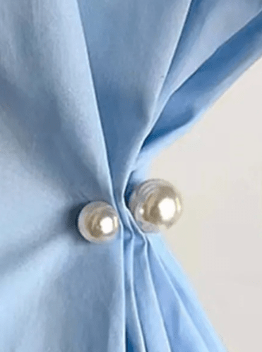 Tøjspænde med to perler, en stor og en lille, fastgjort på lyseblåt stof.